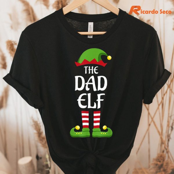 The Dad Elf Christmas T-shirt hanging on a hanger